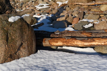 Snow-covered rocky landscape with weathered logs, fallen trees after a hurricane with peeled bark. Storm aftermath