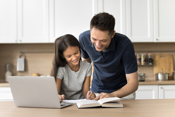 Let me explain. Loving millennial dad support small school age daughter help child with understanding new material from online lesson check homework. Friendly father and kid doing assignment together