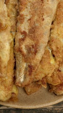 Close-up view of a pile of fried pike-perch fillets coated in flour and egg. Table spin. Vertical video.