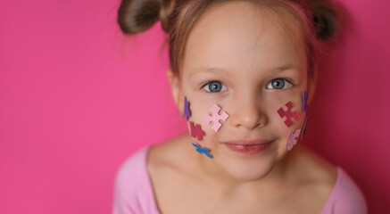 Portrait of a sweet, lovely girl looking at the camera in surprise. A symbol of autism made of colored paper in the shape of puzzles on the cheeks of a child.