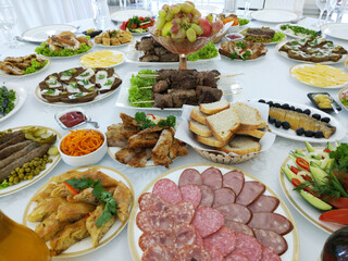 A set table in the hall of a restaurant. on a white tablecloth there are some plates with cold appetizers and some glassware. a festive event. preparation for reception of guests