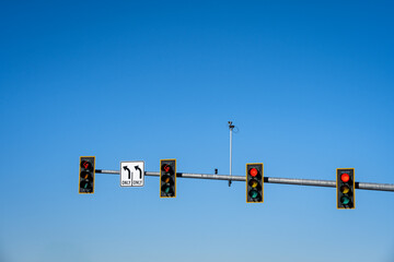 Overhead traffic light for four lanes, two left turn only lanes, sign and red arrow light, and two lanes with red stop light, traffic camera, sunny winter blue sky day

