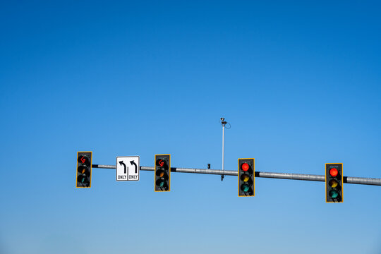 Overhead traffic light for four lanes, two left turn only lanes, sign and red arrow light, and two lanes with red stop light, traffic camera, sunny winter blue sky day
