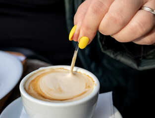 A person stirring a cappuccino with a spoon, close-up on the foam