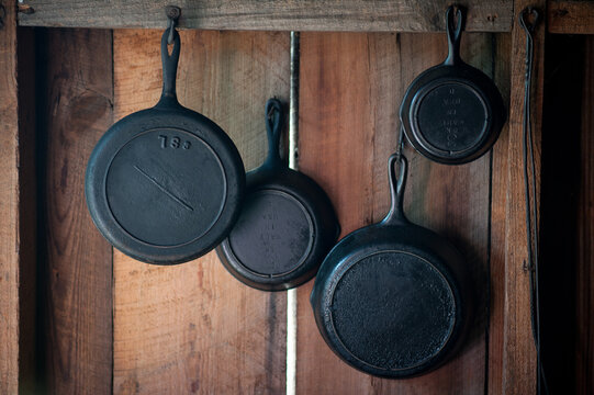 black cast iron pans of different sizes hanging on wooden wall 