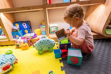 Toddler playing with stacking blocks and colorful toys in an educational playroom