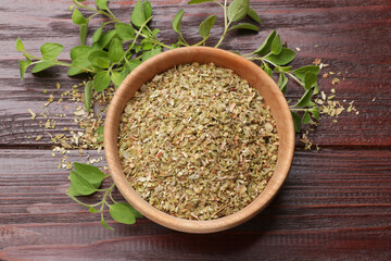 Dried oregano in bowl and green leaves on wooden table, top view