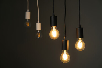 Light bulbs hanging on cords against grey background, selective focus