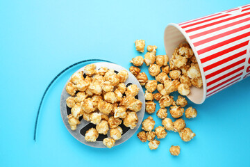 Sweet popcorn and film reel on light blue background, top view. Watching movie