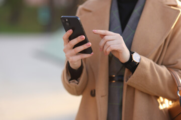 Businesswoman in stylish suit using smartphone outdoors, closeup. Space for text