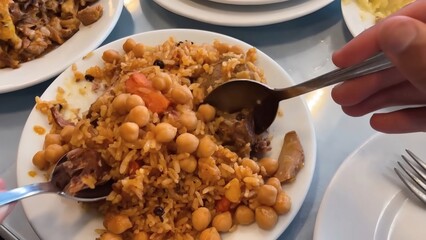 Hands Serving Meat and Rice Pilaf with Chickpeas, Carrots and Raisins on Multiple White Ceramic Plates