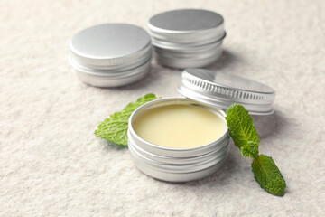 Mint lip balms and green leaves on beige textured table, closeup. Cosmetic product