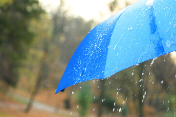 Open blue umbrella under pouring rain outdoors, closeup. Space for text
