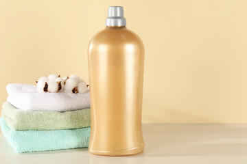 Bottle with laundry detergent, stack of clean towels and cotton flowers on wooden table against beige background