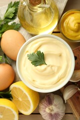 Delicious mayonnaise sauce in bowl and ingredients on wooden table, flat lay