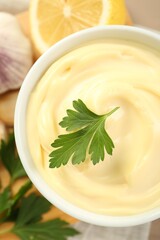 Delicious mayonnaise sauce with parsley in bowl and ingredients on table, top view