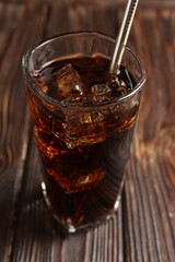 Cold cola with ice cubes and drinking straw in glass on wooden table, closeup