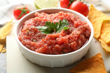 Delicious spicy salsa sauce in bowl and nacho chips on table, closeup
