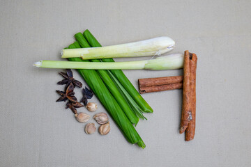 An isolated photo of aromatic spices and herbs, including lemongrass, pandan leaves, cinnamon sticks, star anise, and nutmeg, arranged on a neutral background