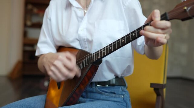 Girl playing acoustic balalaika swiftly with plucking motion at home. Create home music, classic and ethnic musical instruments, practicing memorizing frets and strum. High angle view