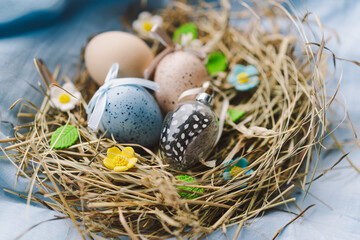 Vibrant Easter eggs are arranged in a cozy nest made of straw, with cheerful flowers contrasting against a soft blue backdrop. This scene captures the festive spirit of spring and Easter concept