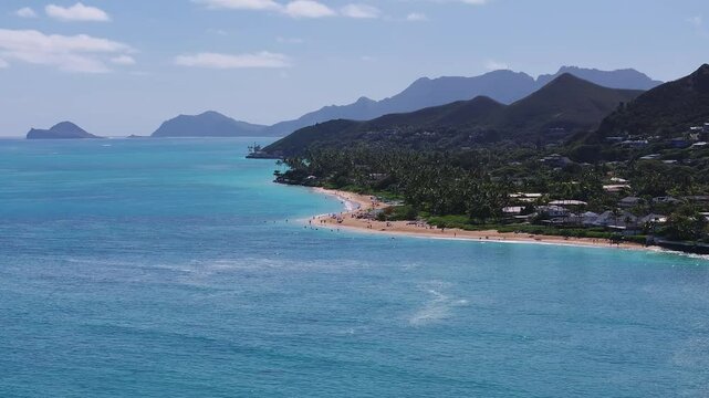 A slow, sweeping aerial pan of Lanikai Beach on Oahu Island, showing turquoise waters, golden sands, Mokulua Islands, and the Ko olau mountain range.