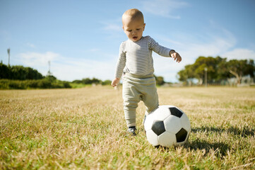 Outdoor, baby and soccer ball on a grass field with mobility development and growth in nature. Child, park and kicking toddler with sport equipment with a kids toy in the summer sun ready to learn