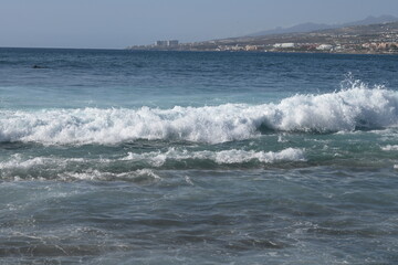 Fototapeta premium Powerful waves breaking in the Atlantic Ocean off the coast of Tenerife, with glistening sunlight illuminating the aqua-green waters.
