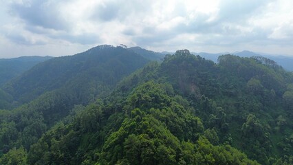 Aerial drone view of lush mountains and hills as well as villages and farmlands with thin morning mist in the morning