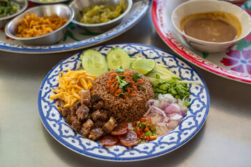 dried shrimp paste fried rice mixed with sausage egg or chopped omelet fresh chili long beans onion mango cucumber lemon and sweet streaky pork in plate with side dishes tray on table by thai food