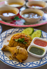 closeup chicken biryani with cucumber sauce yellow rice turmeric and chicken leg in white blue pattern plate with side dishes tray for islamic food or indian cuisine in muslim restaurant on vertical