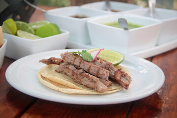 Close-up of a gourmet taco filled with grilled flank steak, topped with cilantro, radish, and a lime wedge, served on a ceramic plate.