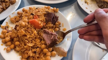 Savory Rice Pilaf with Chickpeas, Carrots, Meat, and Raisins Being Served on Multiple White Plates