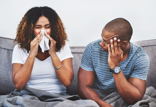 Stress, couple and sick woman in home with sneezing, spread germs and partner frustrated by allergies. African people, risk and tissue for runny nose with viral infection, flu symptoms and sinusitis