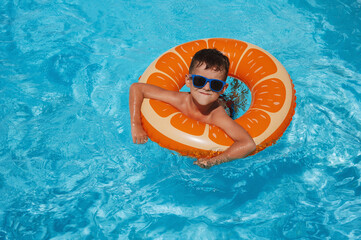 happy small child boy in inflatable circle learns to swim in the swimming pool at a hotel on summer vacation