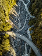 A scenic aerial perspective showing a winding river surrounded by lush green forests and crossed by a bridge with a single car traveling on it, highlighting nature and solitude.