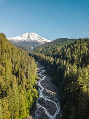 A serene scene featuring a snow-covered mountain, lush coniferous forest, and a winding river flowing through a picturesque valley under a clear blue sky, washington state.