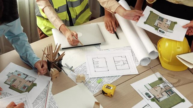 Smart architect and safety engineer discussion about building blueprint on table with architectural document, measurement tools and wooden block scatter around at modern office. Closeup. Delineation.