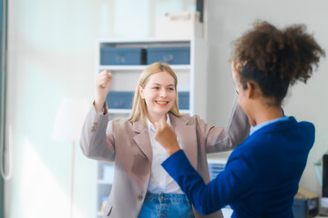 Two young women, an African American and a Russian, both wearing formal suits, collaborate in a modern business office, consulting financial charts,  engaging in professional discussions.