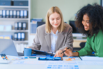 A young African American woman and a young Russian woman work together in a business office. They...