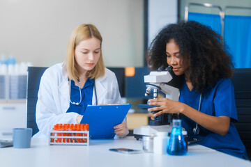 Young African American and Russian woman, both scientists, collaborate to analyze blood samples,...
