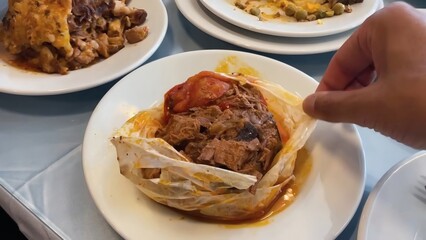Hand Peeling Back Parchment Paper to Reveal Tender Meat on a White Plate in a Multi-Course Meal