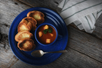 High angle shot of  blue mug filled with fresh homemade tomato soup. on a matching blue plate, on a rustic wood background with dramatic side light.