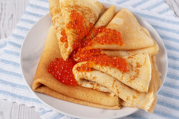 Freshly made crepes topped with vibrant fish roe served on a striped cloth in a cozy kitchen setting