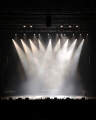 A dimly lit stage is illuminated by multiple beams of light, creating an atmosphere of anticipation for a performance.