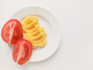 Mashed potatoes and tomato slices in a white plate on a white table, top view, text space on the right side. The menu in the dining room, restaurant. Garnish. Promotional photo for a vegetarian restau