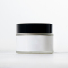 A clear jar with a black lid on a plain background, perfect for modern skincare or cosmetic use