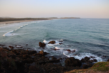  A panoramic view of a coastal landscape with sandy beach, crashing waves, and rocky shoreline 