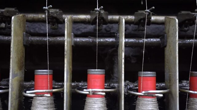 A close-up of a spinning machine at rest, showing flax yarn spools with tensioned threads. The industrial setup highlights the precision and mechanics involved in textile production.