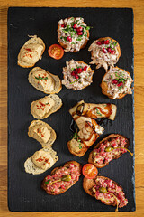 A vibrant array of tapas adorns a black stone platter, featuring artfully arranged spreads, toppings, and garnishes—ideal for sharing at a cozy gathering. 